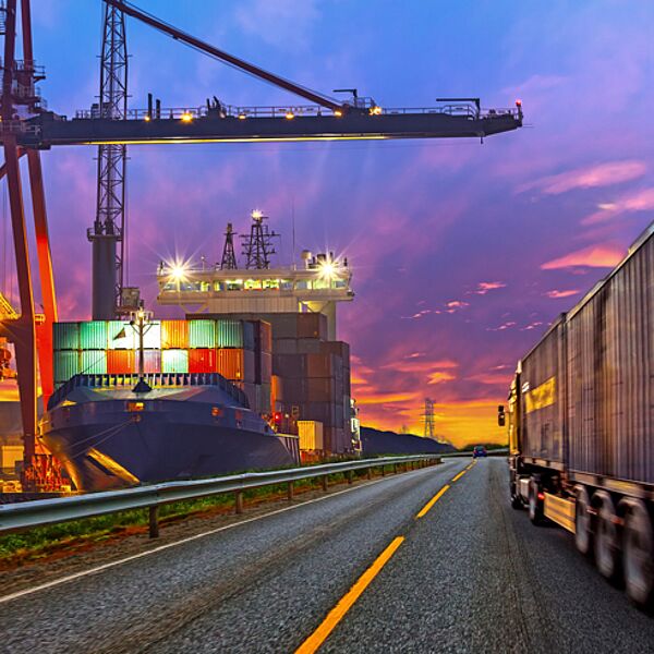 uhlhorn-kontraktlogistik-hafen-lkw-transport Uhlhorn Kontraktlogistik – LKW fährt am Hafen vorbei, Containerschiff bei Abenddämmerung, multimodale Transportkette.